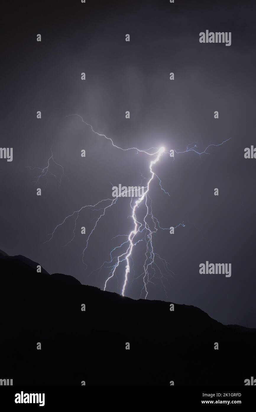 A vertical shot of lightning striking at night on hills Stock Photo