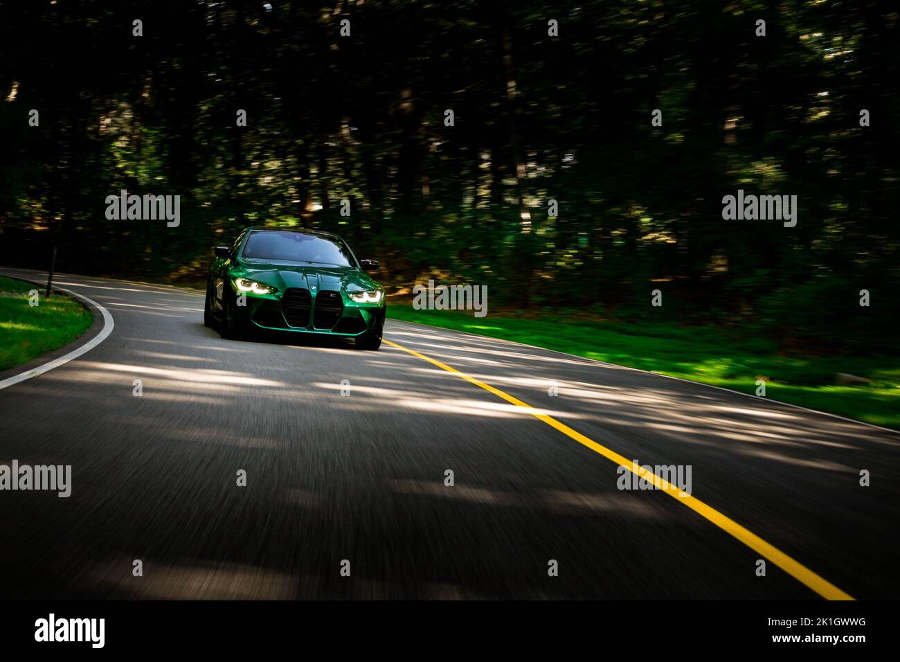 Rolling shot of BMW M4 Performance on asphalt road with trees blurring by in the background Stock Photo