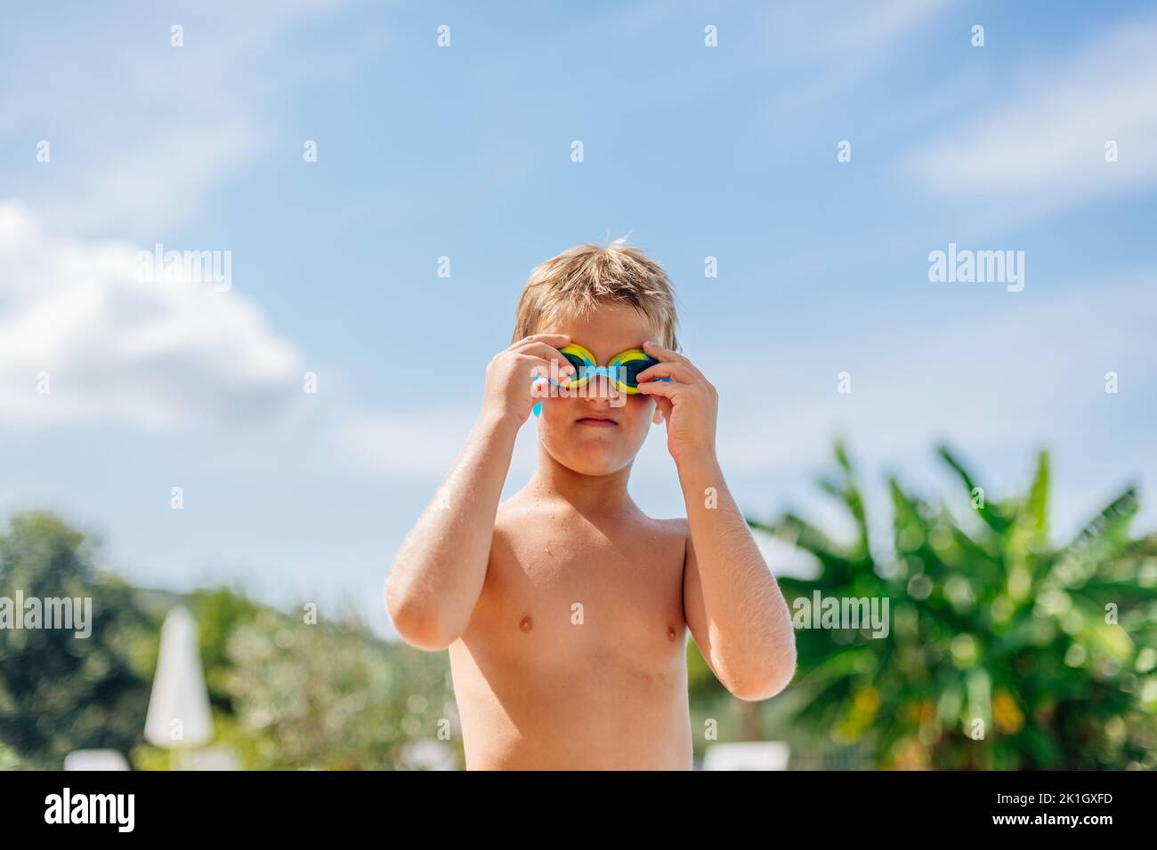 8-year-old boy puts on his swimming goggles and gets ready to swim in the hotel's swimming pool. Stock Photo