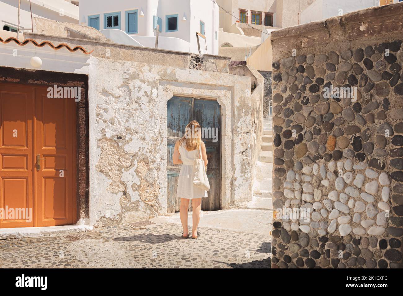 A young blonde female tourist explores and wanders throough the traditional old town cobblestone streets in the quaint, charming village of Pyrgos Kal Stock Photo