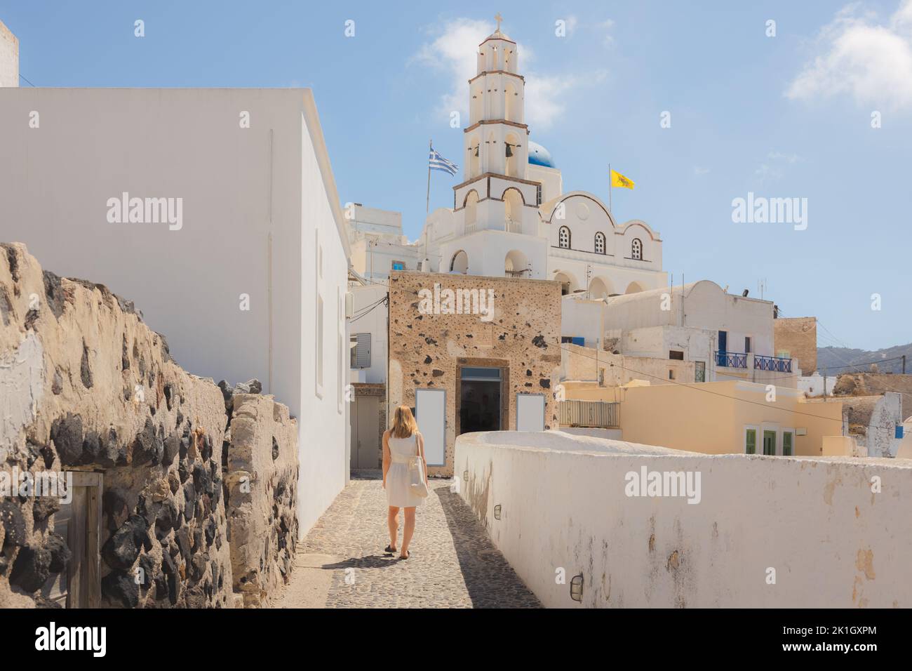 A young blonde female tourist explores the traditional old town cobblestone streets in the quaint, charming village of Pyrgos Kallistis towards with t Stock Photo