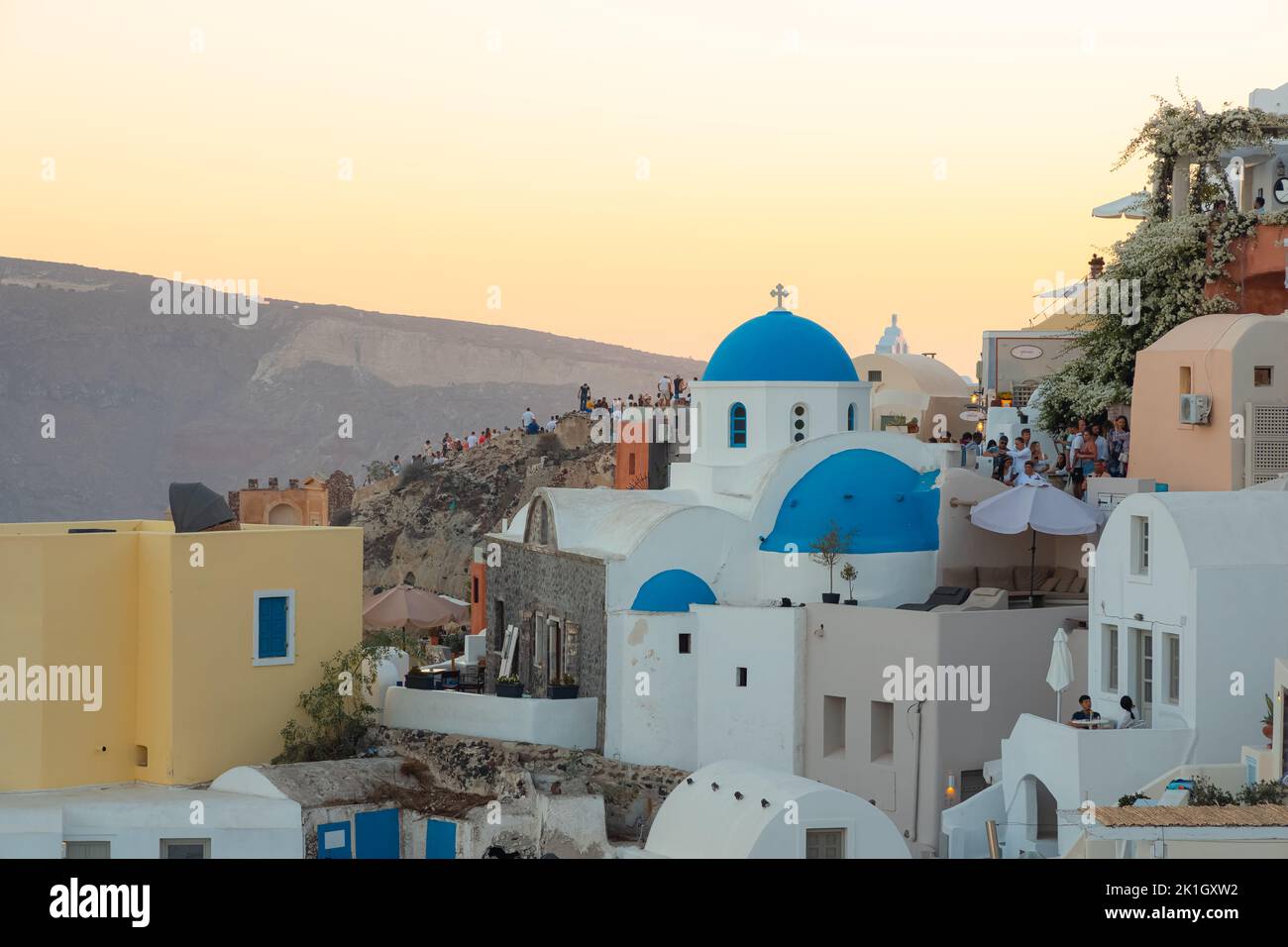 Oia, Greece - September 11 2022: Sunset view of traditional white wash buildings and blue dome church Panagia Agion Panton at the popular seaside tour Stock Photo