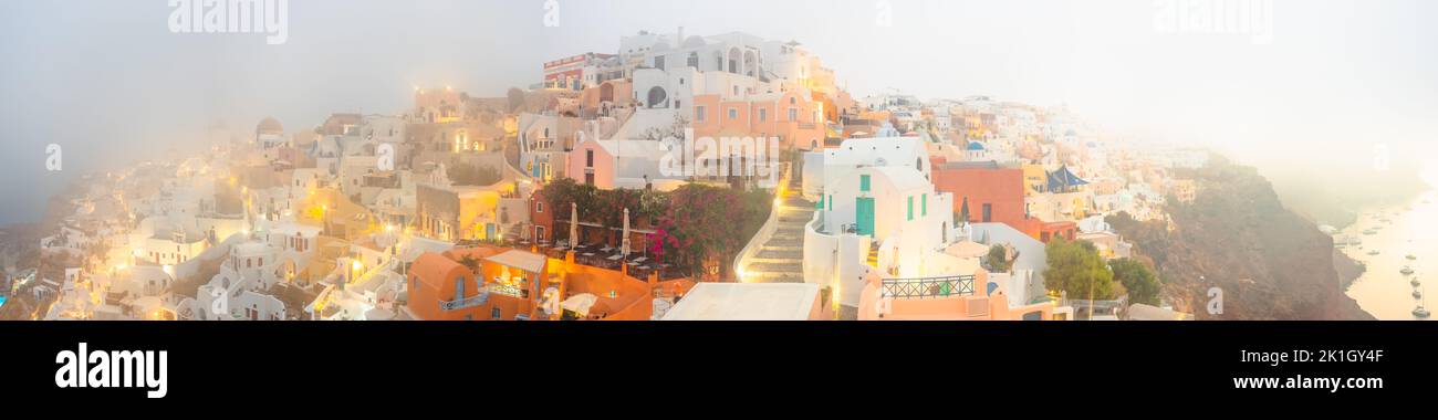 Wide panoramic view at blue hour on a foggy, misty morning at the popular seaside tourist resort village of Oia on the Greek island of Santorini, Gree Stock Photo