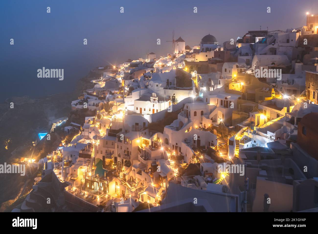 Seaside view at blue hour of traditional white wash buildings and windmill on a foggy, misty morning at the popular seaside tourist resort village of Stock Photo