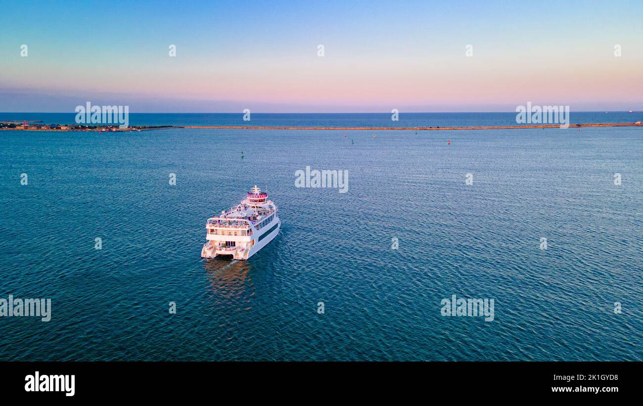 Aerial view of a harbor with ships sailing and docked. Photography was taken from a drone at a higher altitude in summer season at sunset. Stock Photo