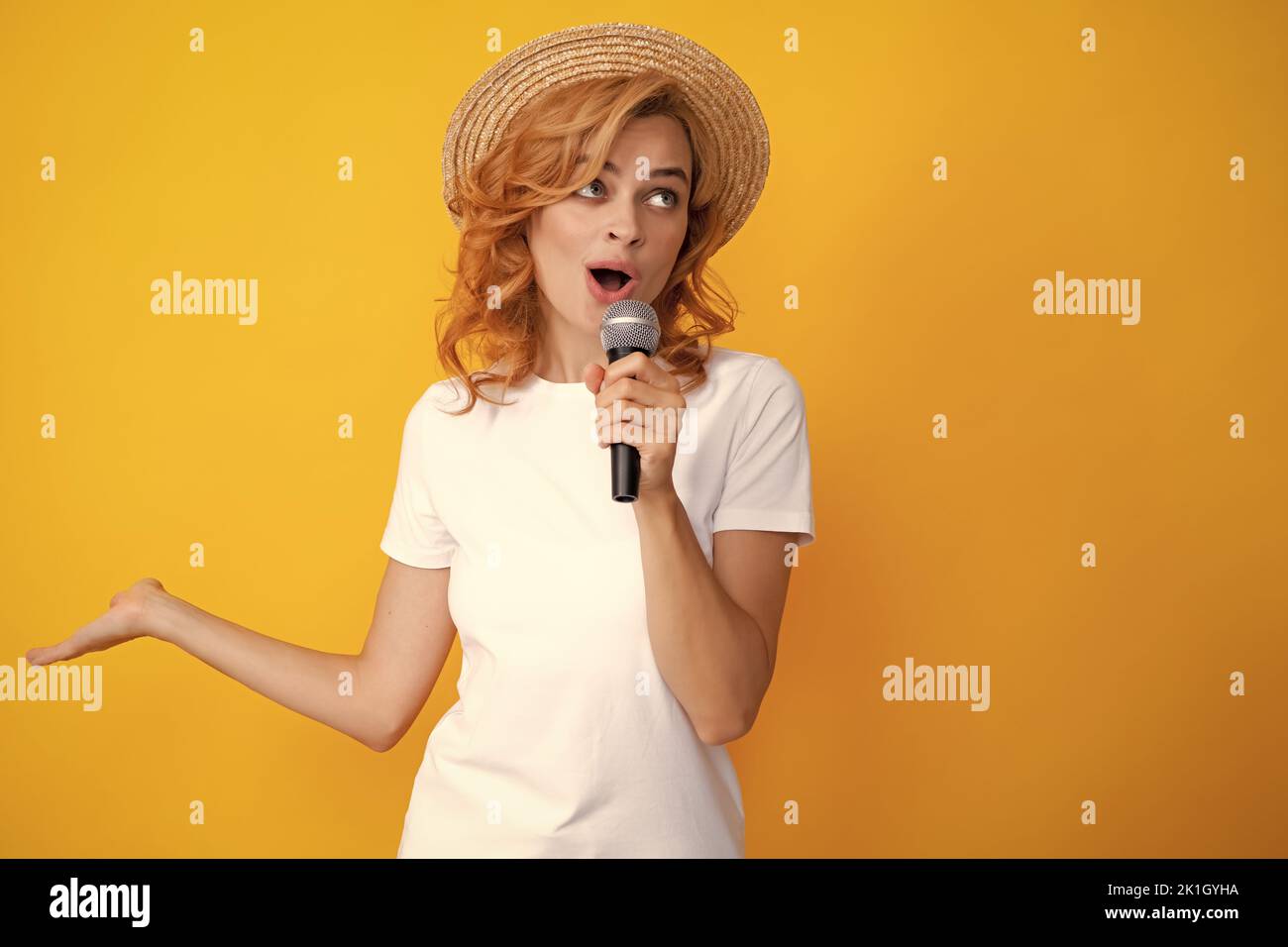 Young woman talking in microphone, perfom with mic, giving speech, standing on yellow background. Stock Photo