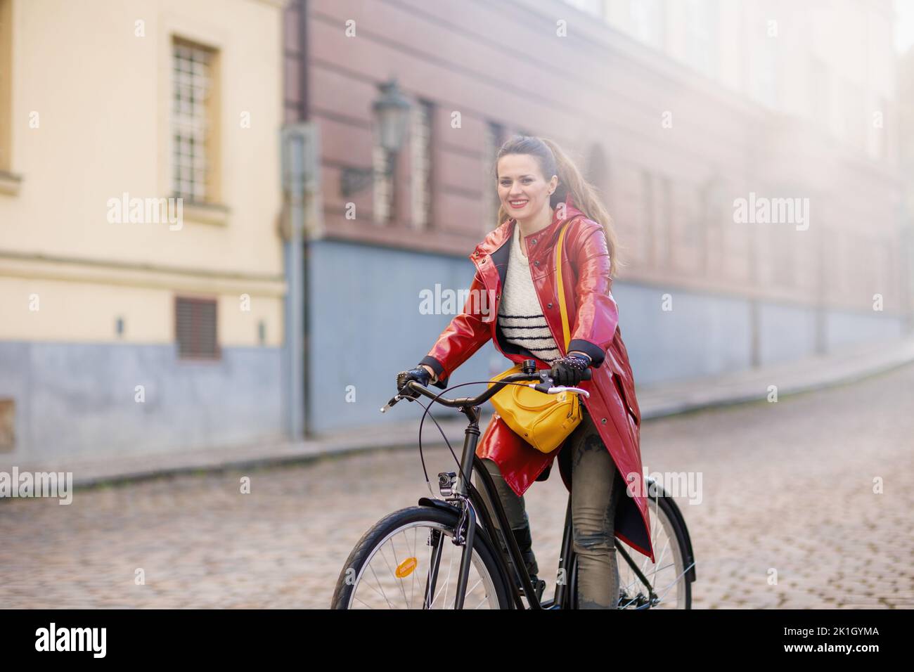 smiling modern middle aged woman in red rain coat outdoors on the city ...