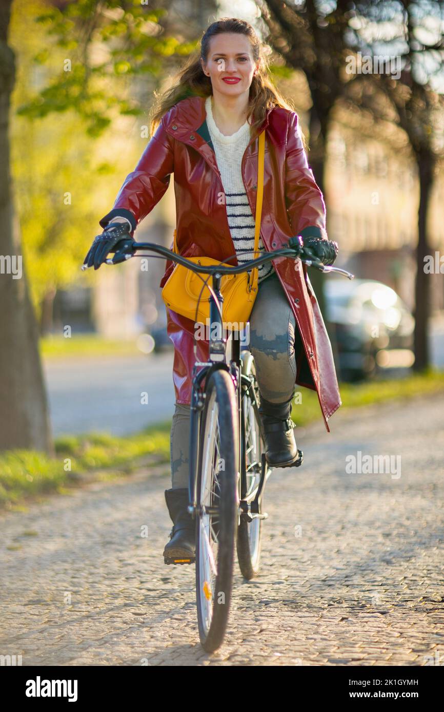 happy stylish woman in red rain coat outdoors in the city riding ...
