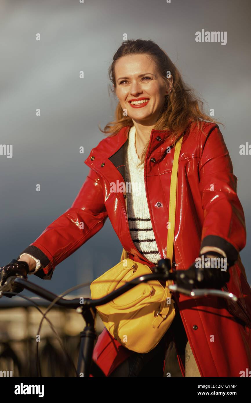 smiling modern female in red rain coat outside on the city street ...