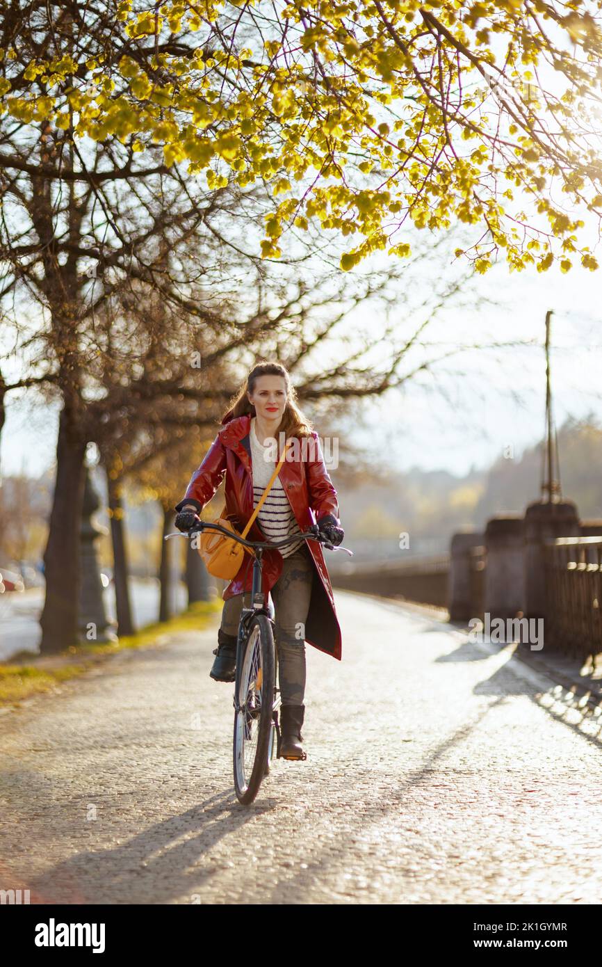 happy stylish middle aged woman in red rain coat outdoors on the city ...