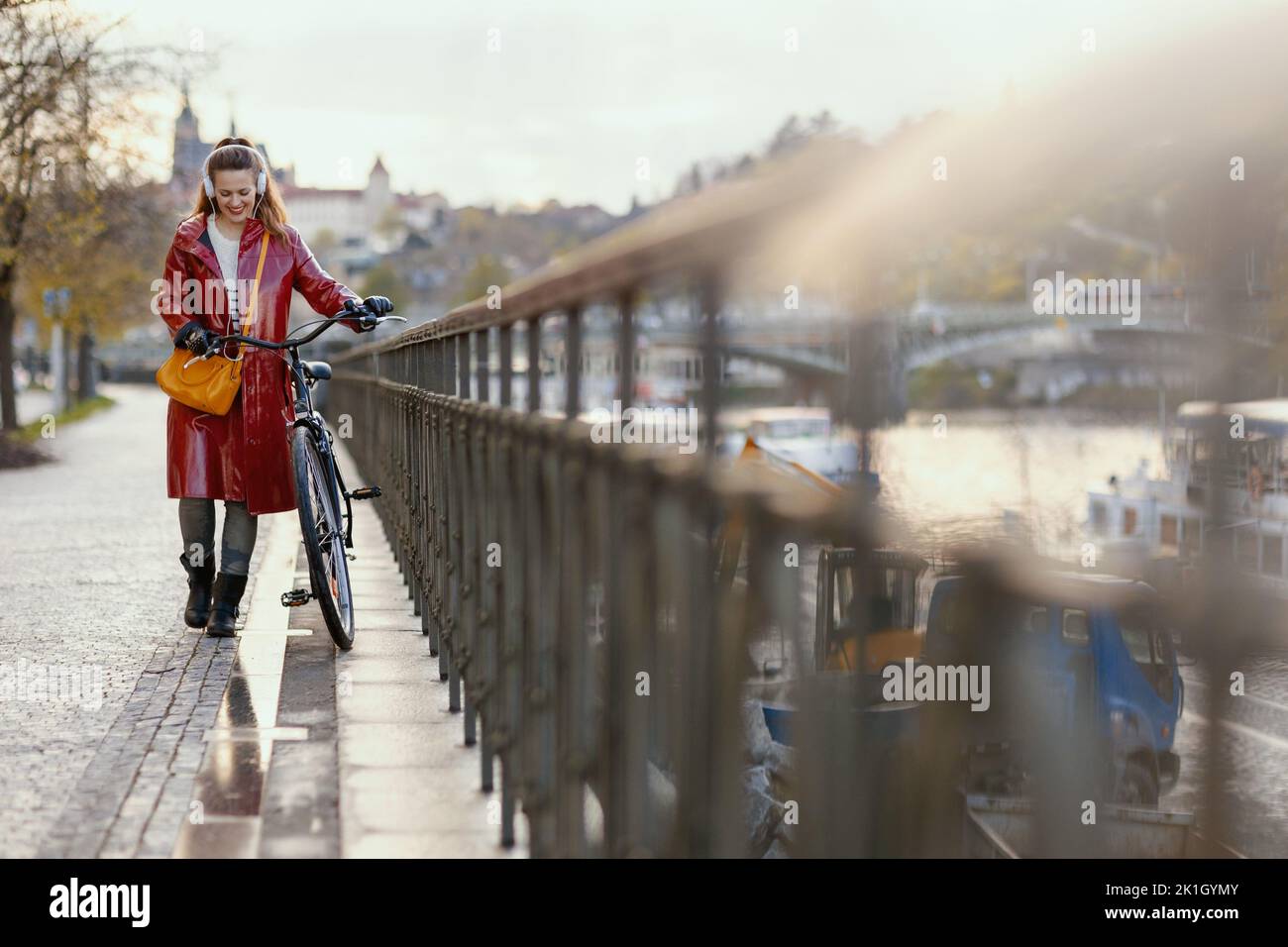 happy modern middle aged woman in red rain coat with bicycle walking ...