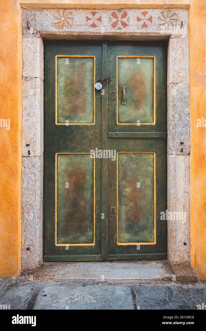 Detail of a traditional and decorative, green, yellow and gold door in with stone motifs in the frame in the old town village of Oia on the Greek Isla Stock Photo