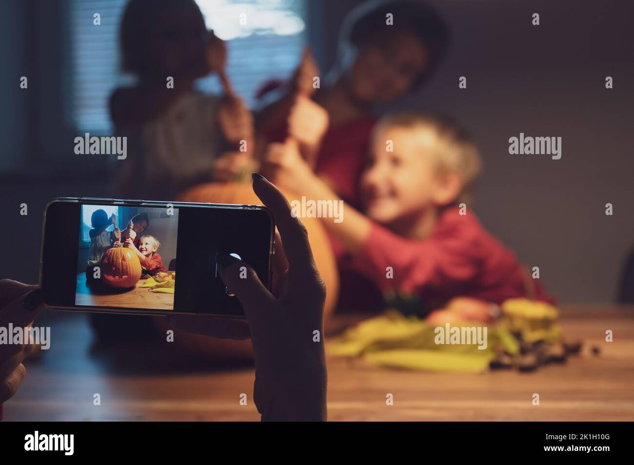 Mother using her mobile phone to take photos of her excited three kids with a halloween pumpkin they had carved. Stock Photo