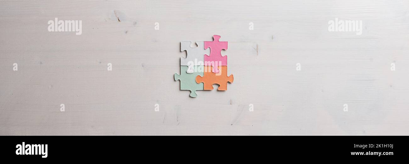 Wide view image if four blank puzzle pieces of various pastel colours joined together over wooden background. Stock Photo