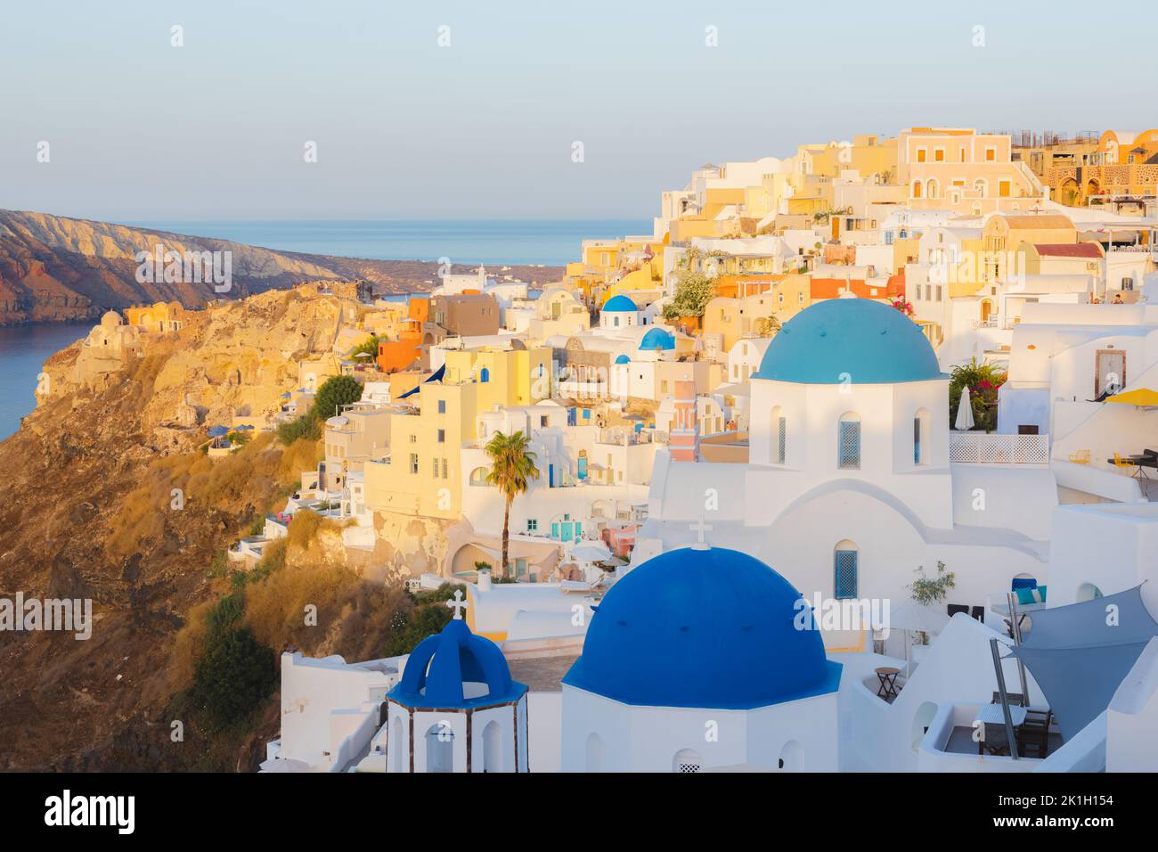 Golden hour sunlight over traditional white wash buildings and colourful blue dome churches at the popular seaside tourist resort village of Oia on th Stock Photo