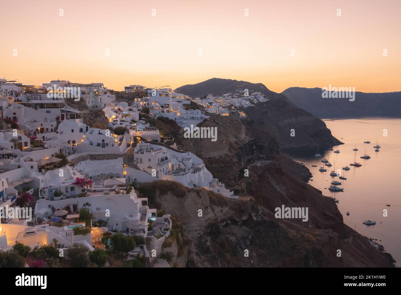 The hilltop village of Oia atop dramatic volcanic rock coastline over the Aegean Sea at sunset or sunrise on the Greek island of Santorini, Greece. Stock Photo