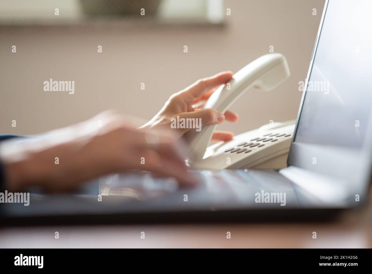 Closeup view of busy caucasian businesswoman typing on laptop computer while also making a call using classical white landline telephone. Stock Photo