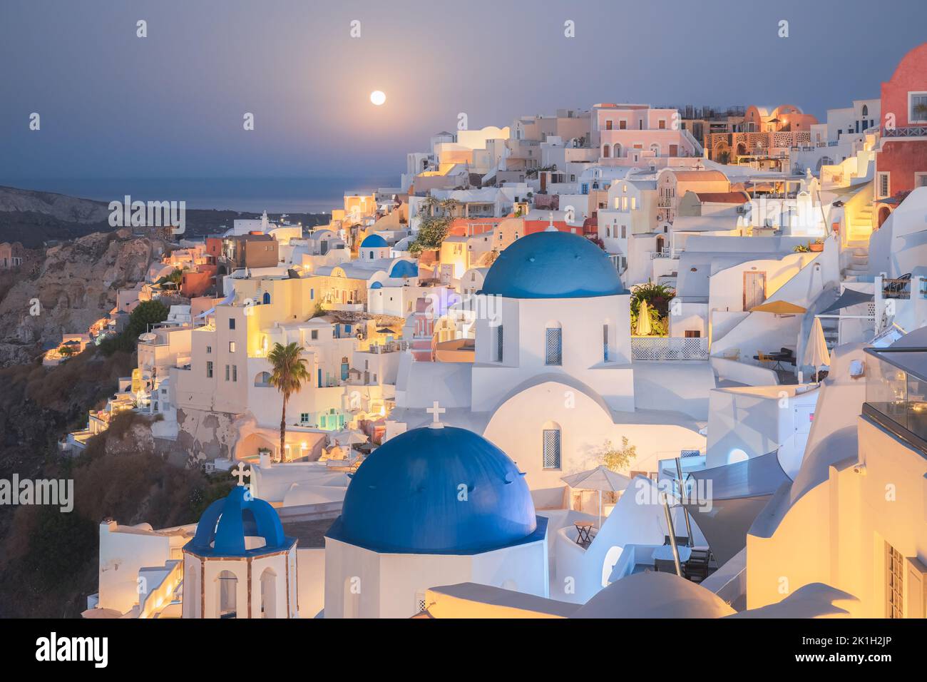 Seaside moonlit view at night of traditional white wash buildings and blue dome churches at the popular seaside tourist resort village of Oia on the G Stock Photo