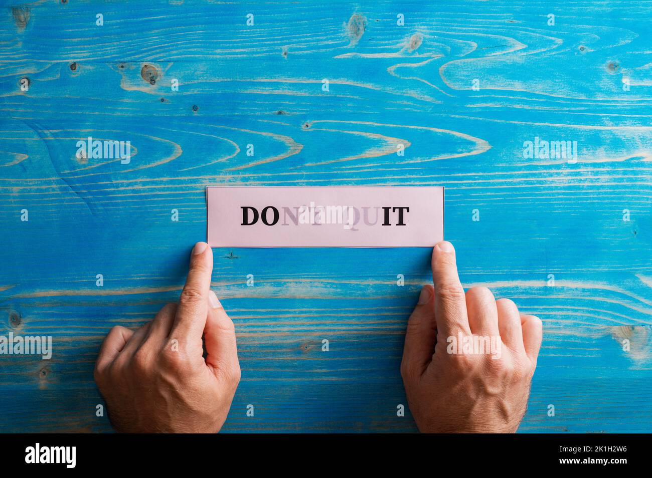 Male hands holding a paper with Dont quit sign fading into a Do it sign written on it, placing it on textured blue background. Stock Photo