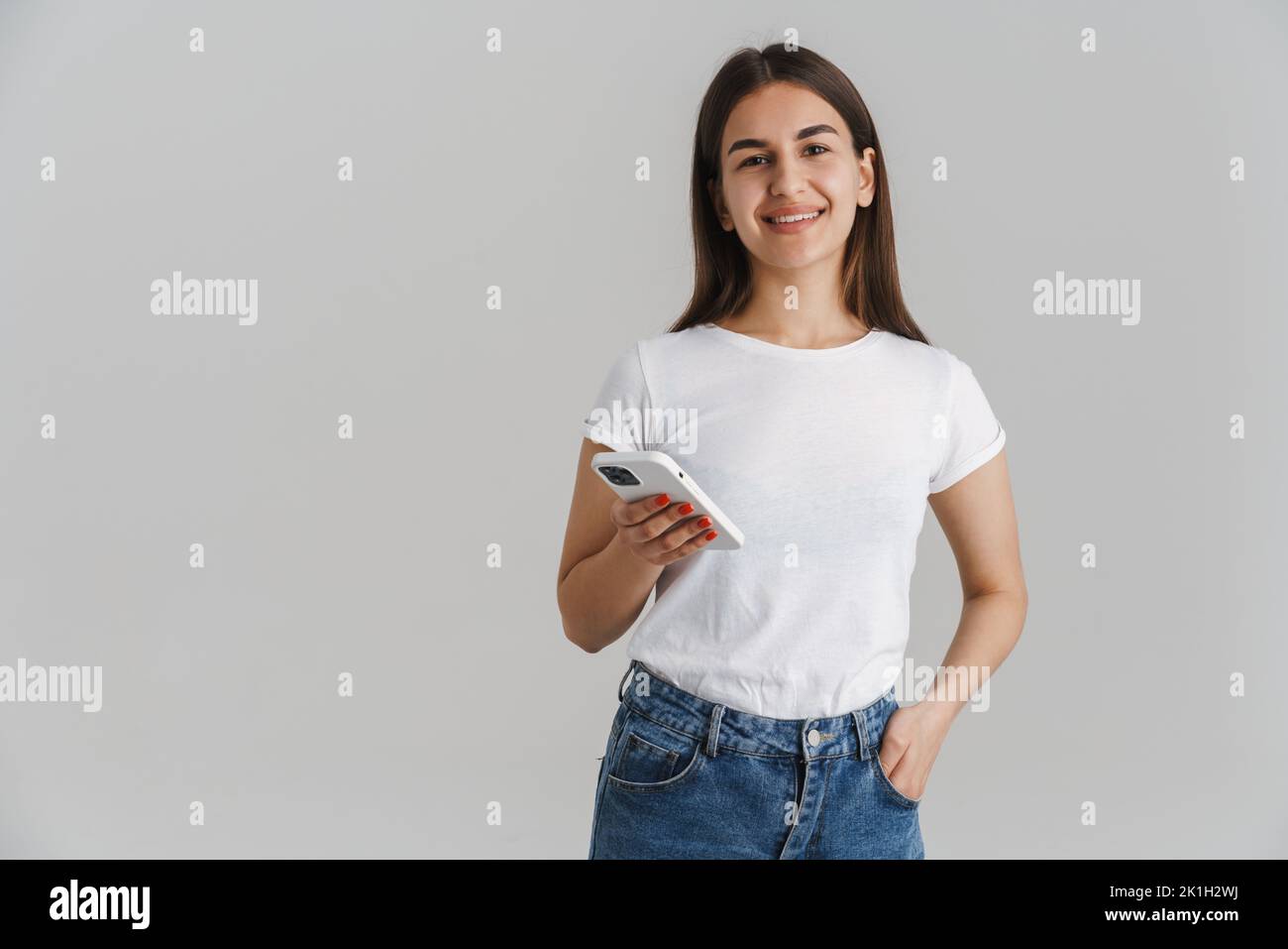 Portrait of a young happy casual white woman in t-shirt with long brunette hair standing over gray wall background Stock Photo