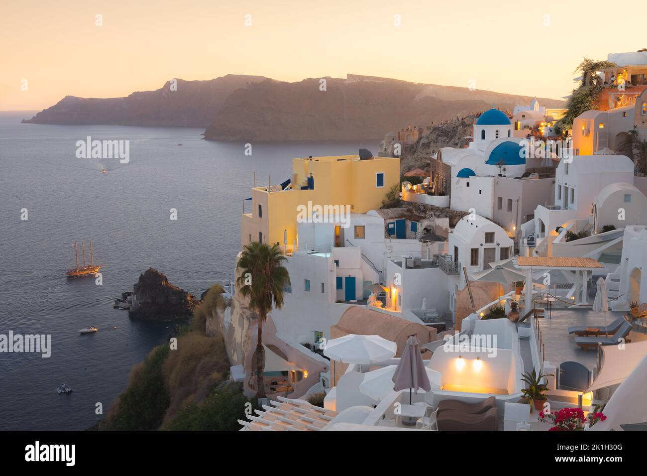Seaside view at sunset of traditional white wash buildings and blue dome church at the popular seaside tourist resort village of Oia on the Greek isla Stock Photo