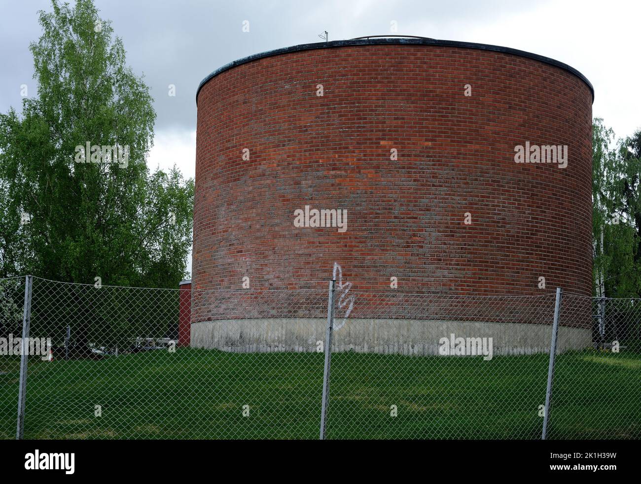 cylindrical brick building behind a mesh metal fence, deadpan photography Stock Photo
