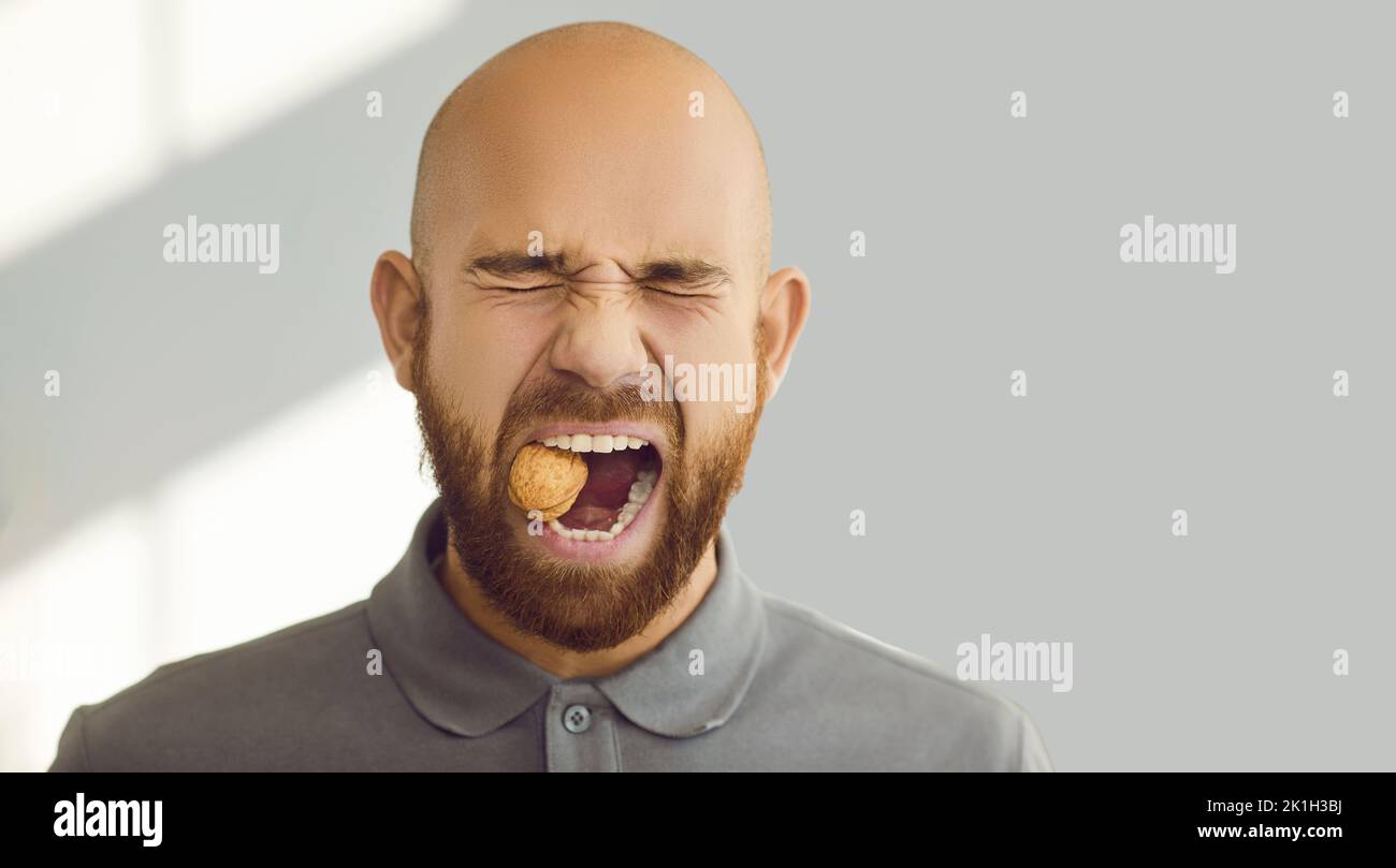 Man with strong healthy teeth trying to crack walnut while standing on gray background. Stock Photo