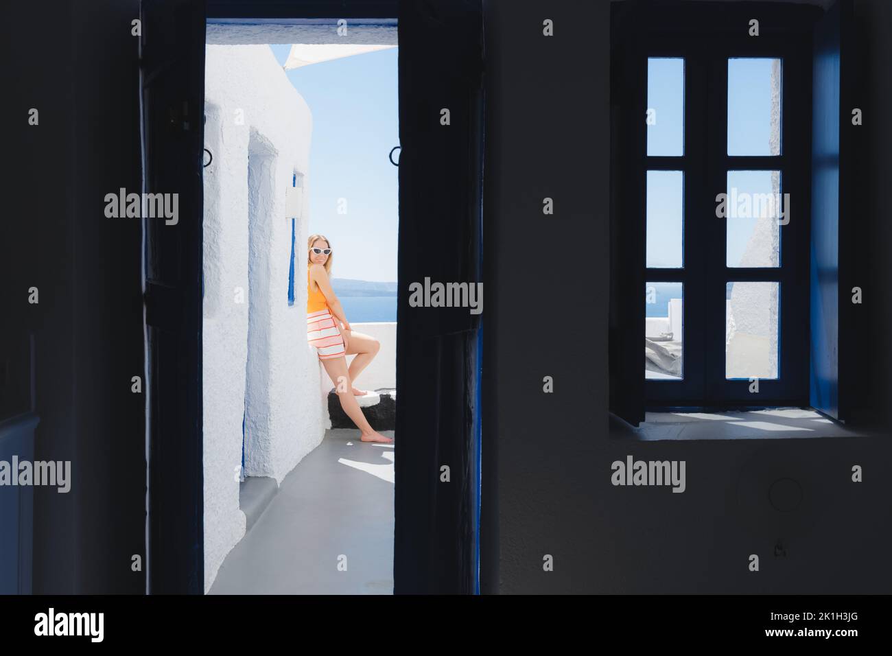 A young blonde female tourist enjoying the patio at a Greek villa on summer vacation in the holiday village of Oia on the island of Santorini, Greece. Stock Photo