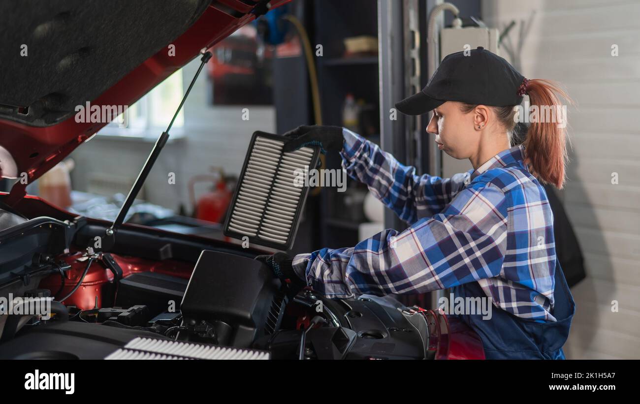 Caucasian female auto mechanic changes the engine air filter in the car. Stock Photo