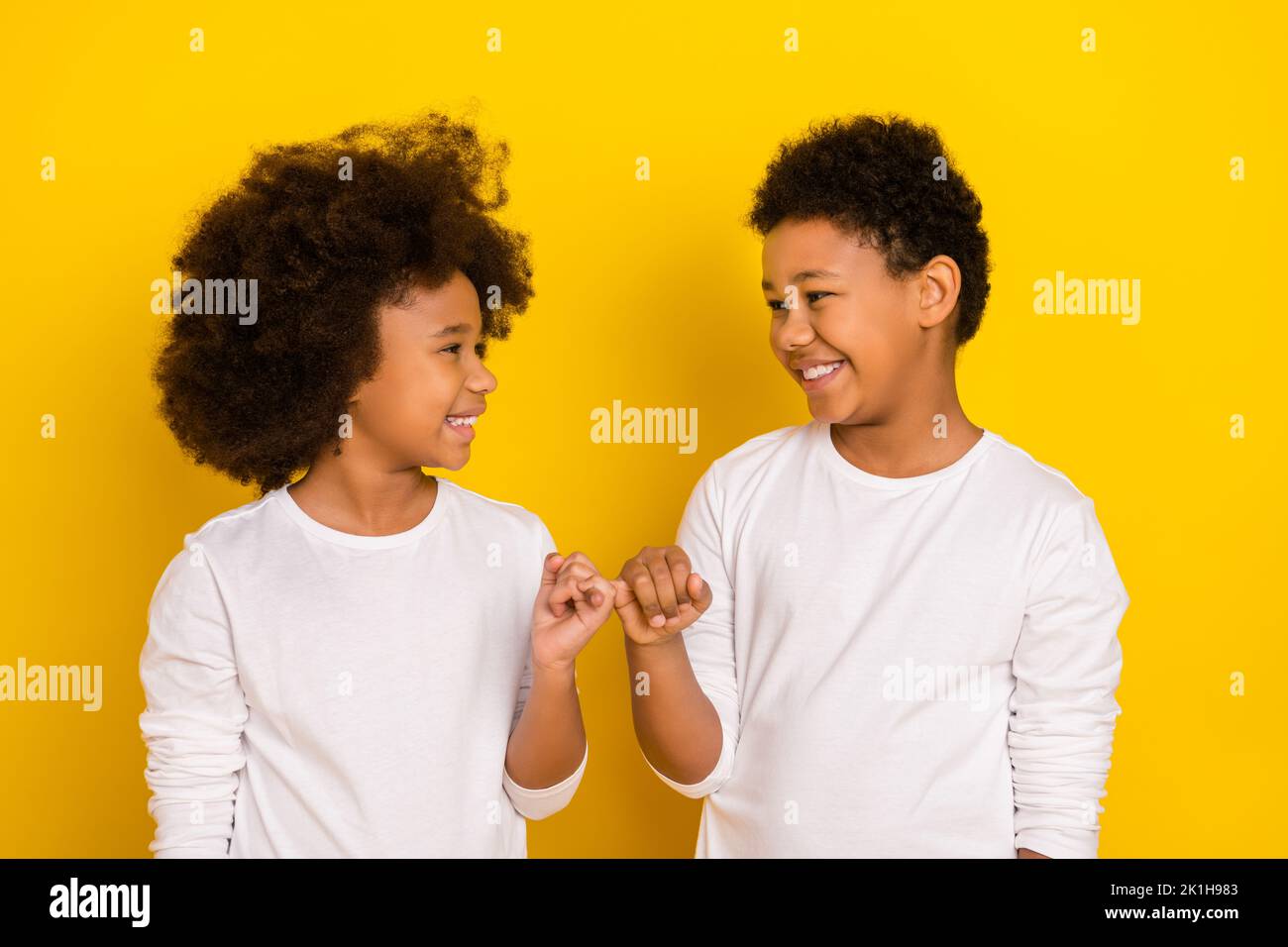 Photo of sweet friendly schoolboy schoolgirl wear white shirts holding small fingers isolated yellow color background Stock Photo