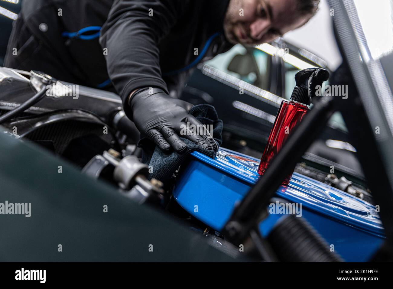 Car mechanic or car wash worker will clean the car engine with a cloth