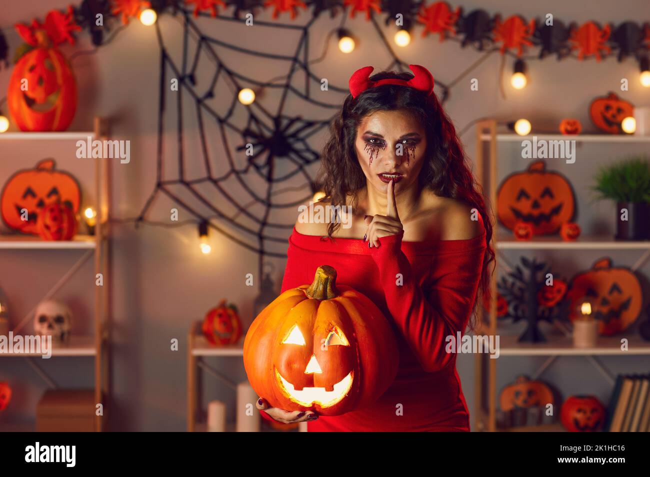 Woman dressed up as devil doing Shh finger on lip gesture at secret Halloween party Stock Photo