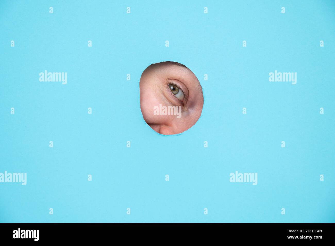 Woman peeking out of hole in blue paper background.  Stock Photo