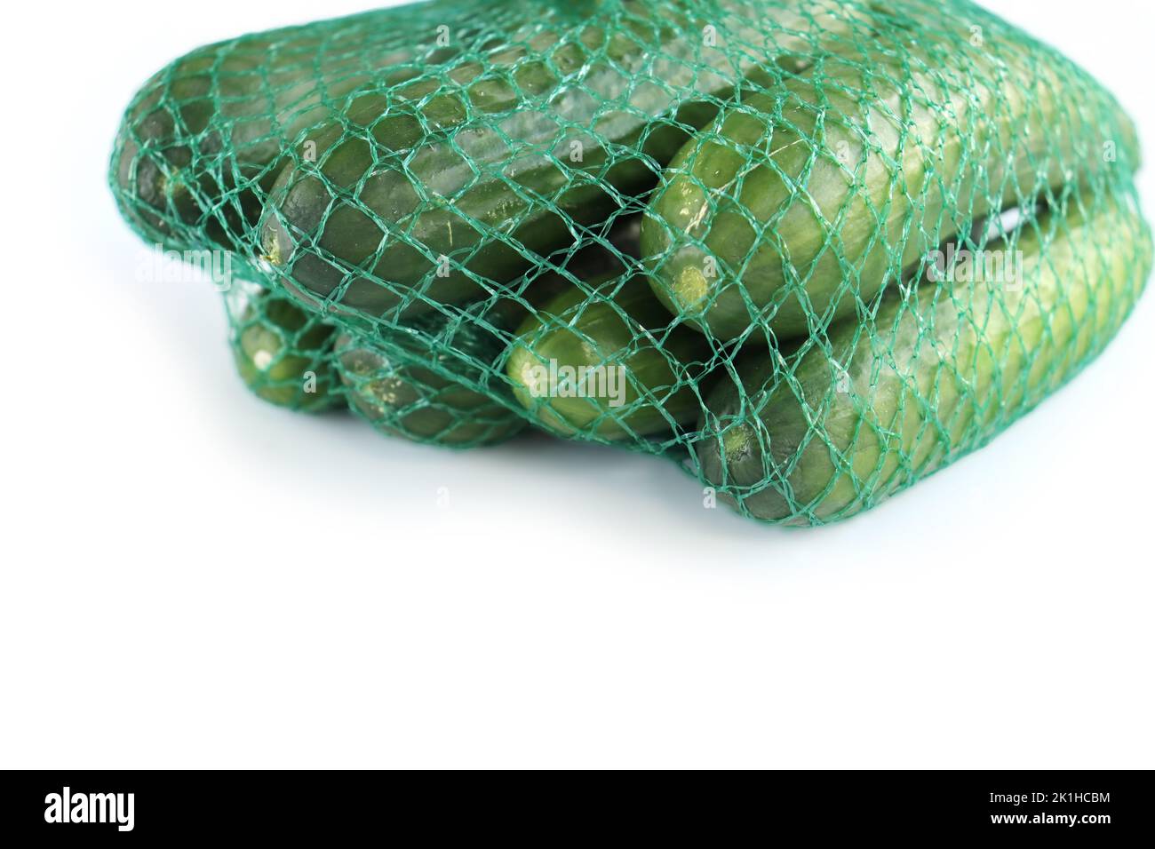 A pile / heap of green cucumbers in the green plastic net mesh / bag. Isolated on the White background. Space for text. Copy space. Top view. Side vie Stock Photo