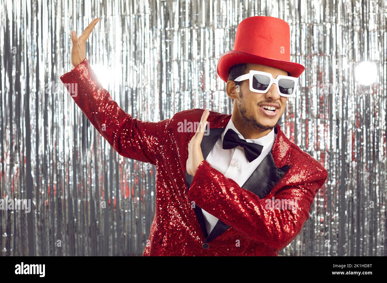 Happy funny black man in a red sequin jacket, top hat and sunglasses dancing at a party Stock Photo