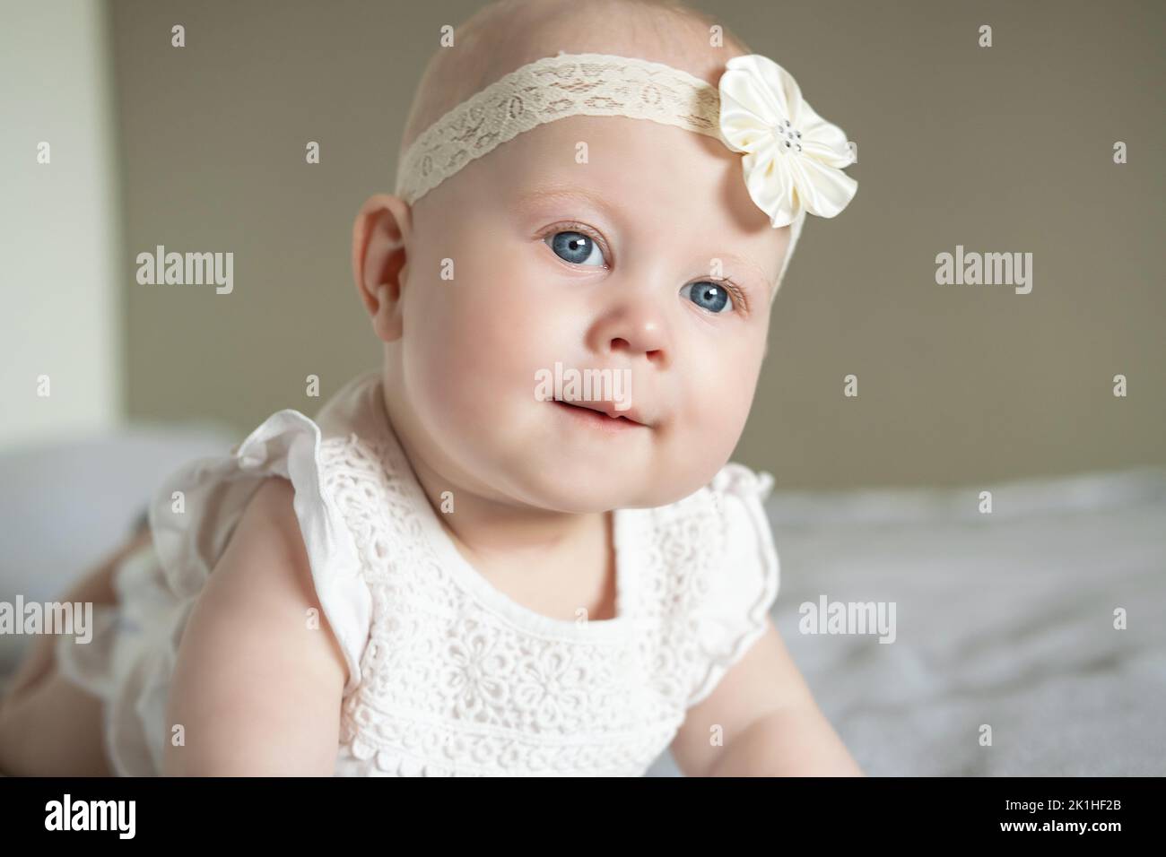 Portrait of a beautiful little baby girl lying on her stomach and looks away with admiration. Baby with big blue eyes. happy family concept Stock Photo