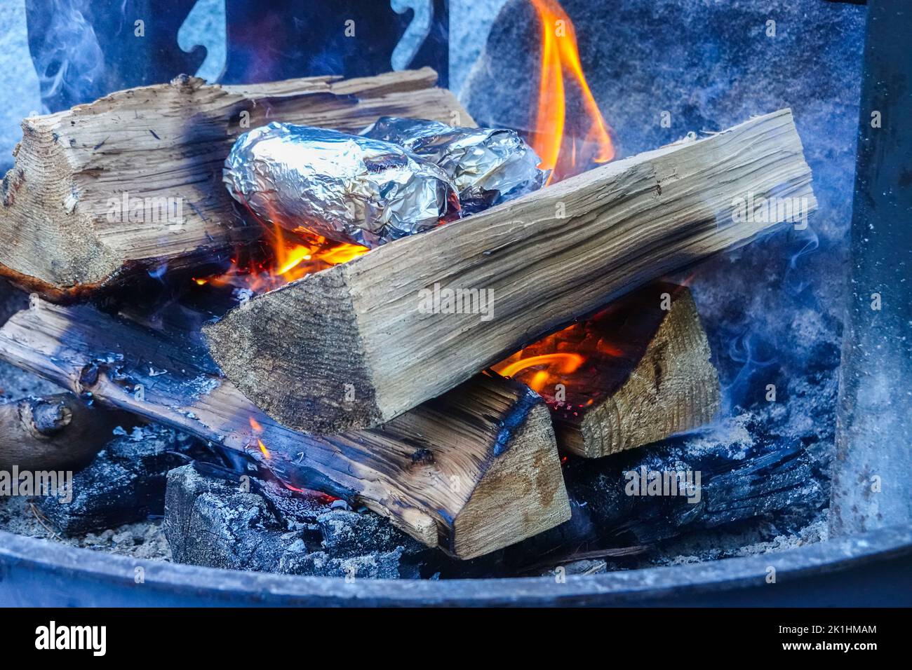 Baked potatoes cooking over a Wood campfire wrapped in foil. Stock Photo