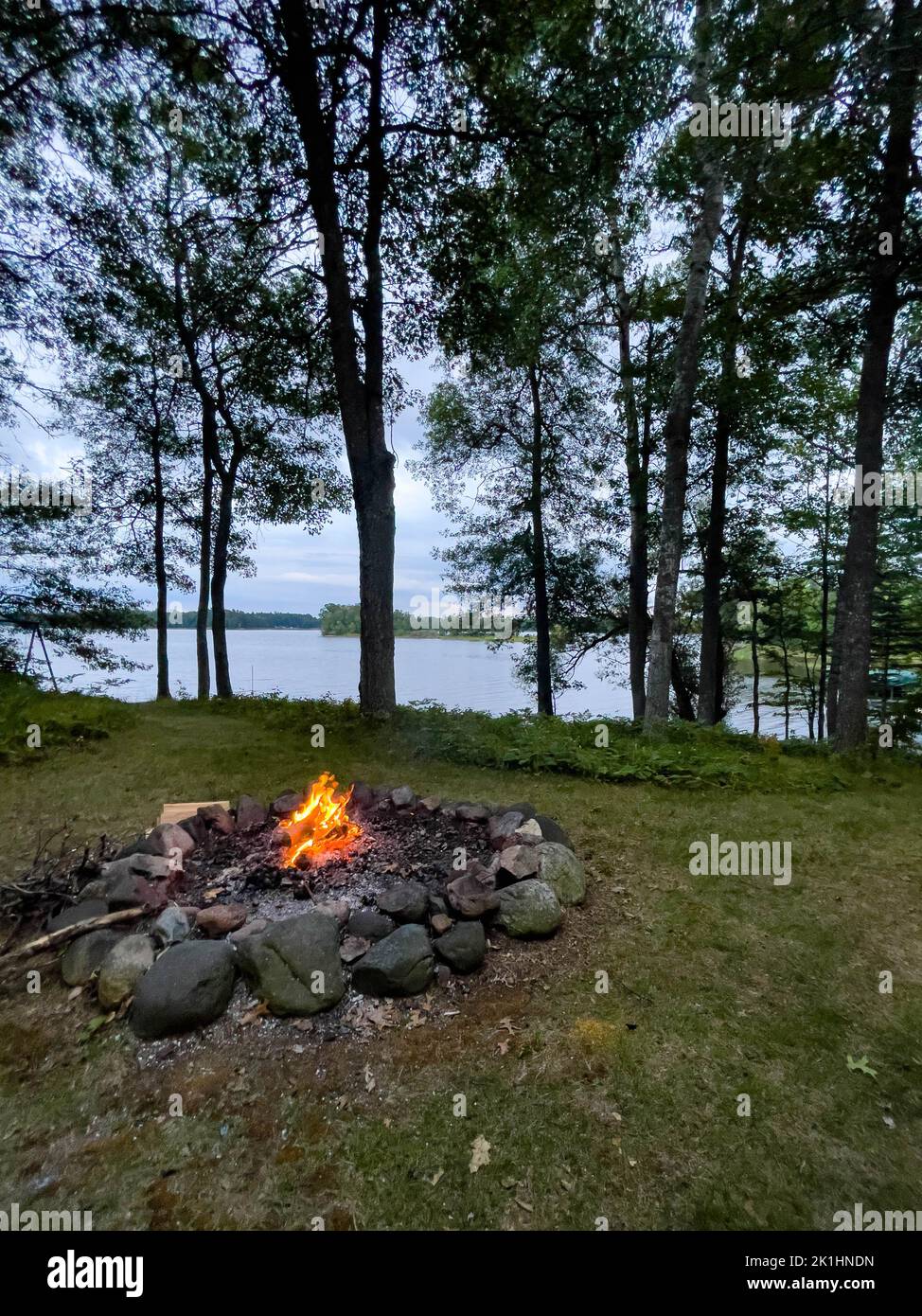 Campfire next to a calm lake in the summer, vertical Stock Photo