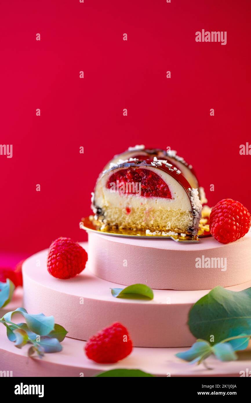 Berry cake with raspberry filling cut and raspberries on a pink podium on a bright red background.Delicate airy cake souffle Stock Photo