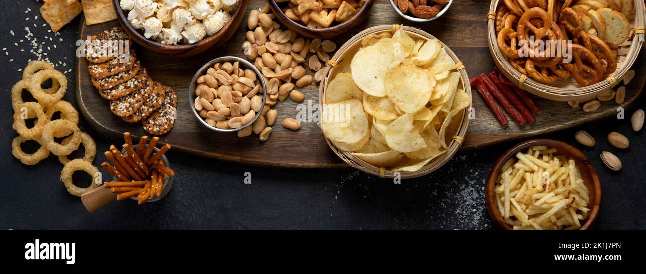 Assortment of salty snacks on dark background. Party food concept. Top view, panorama, copy space Stock Photo