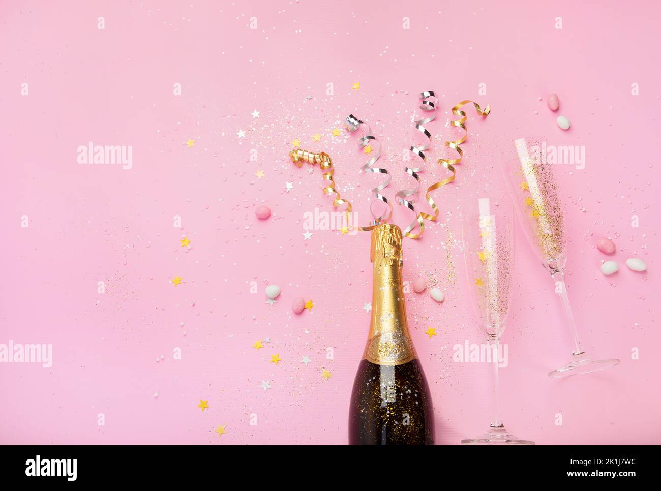 Champagne bottle with confetti on pink background. Holiday decoration and party streamers on gold festive. Creative concept. Top view, copy space Stock Photo