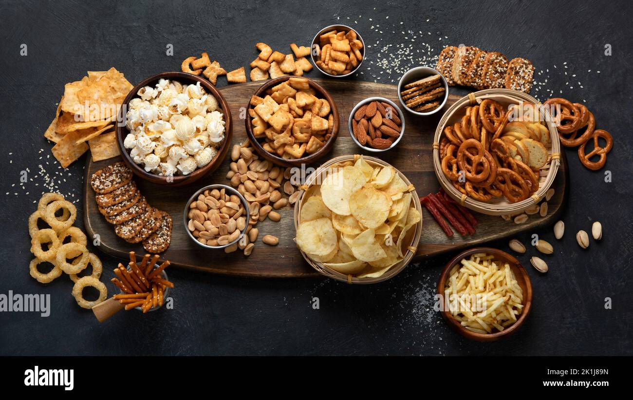 Assortment of salty snacks on dark background. Party food concept. Top view Stock Photo