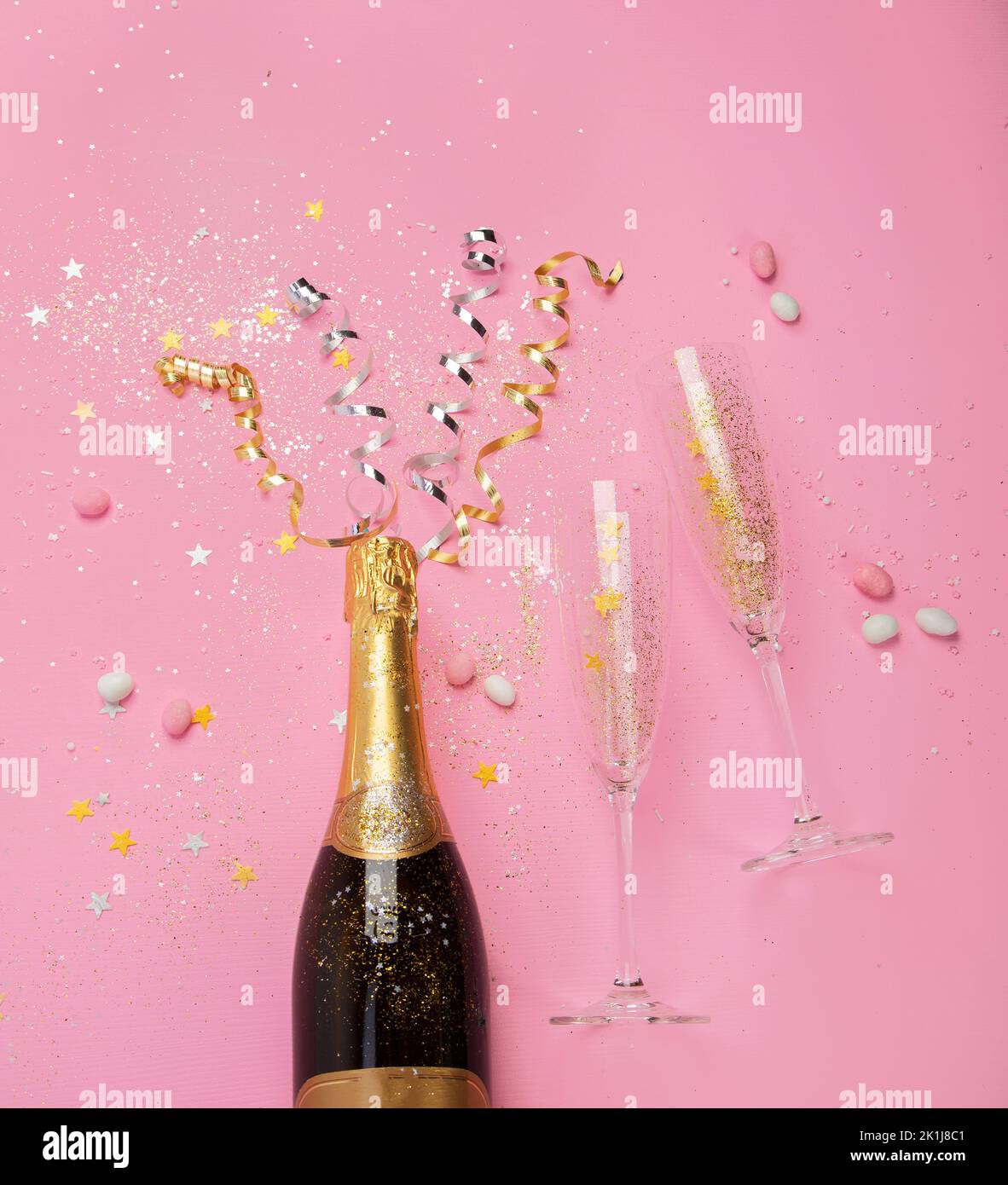 Champagne bottle with confetti on pink background. Holiday decoration and party streamers on gold festive. Creative concept. Top view Stock Photo