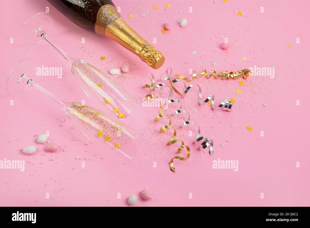 Champagne bottle with confetti on pink background. Holiday decoration and party streamers on gold festive. Creative concept. Stock Photo