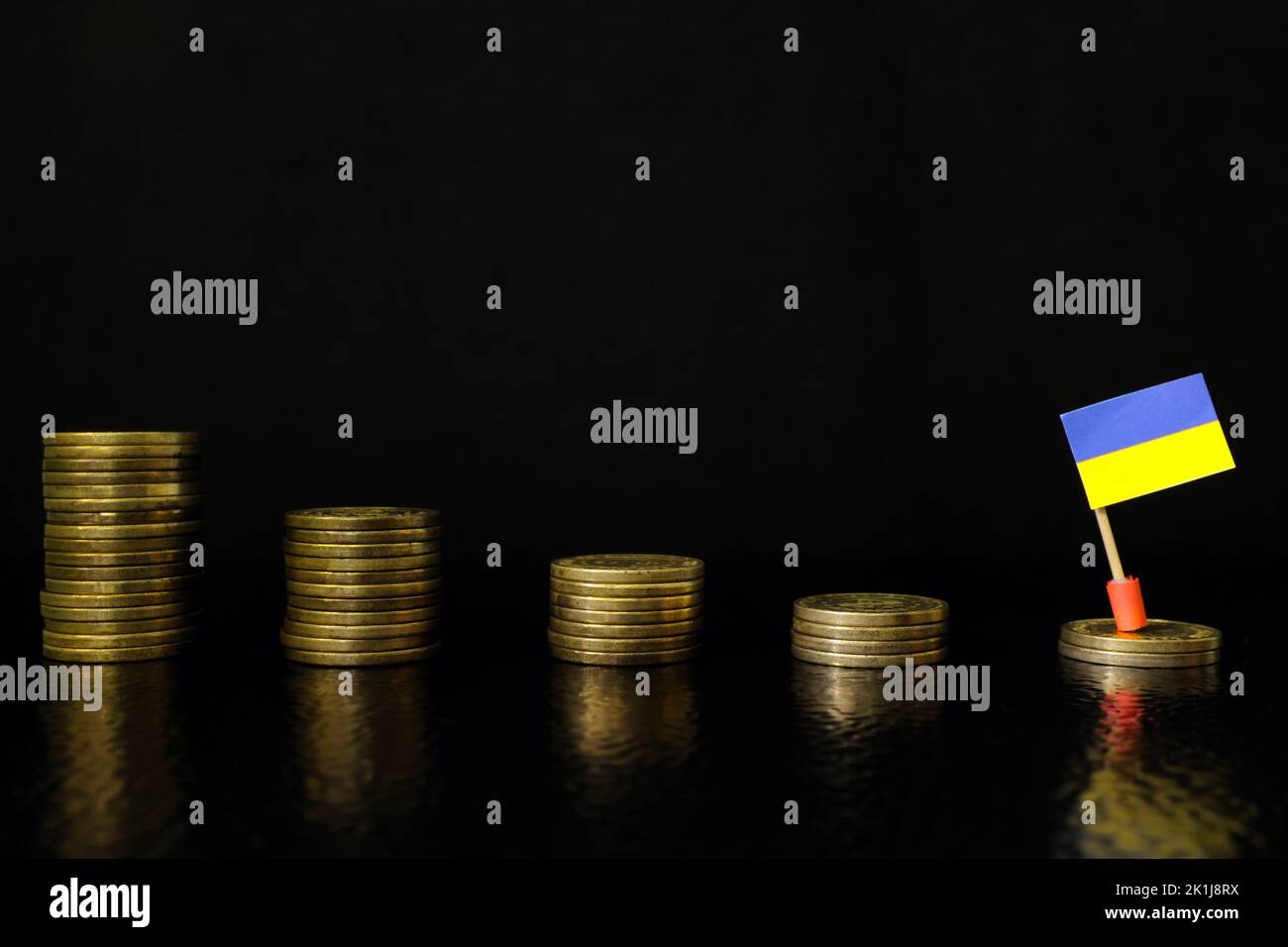 Ukraine economic recession, financial crisis and currency depreciation concept. Ukrainian flag in decreasing stack of coins in dark black background. Stock Photo