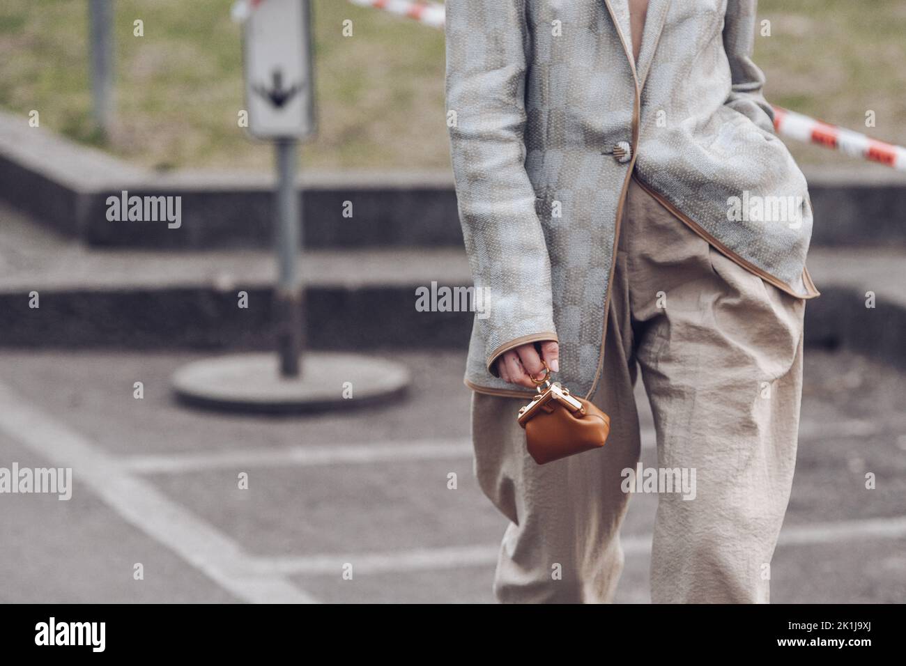 Milan, Italy - February, 24: Street style, woman wearing silver blazer jacket, beige large pants, a brown shiny leather micro First handbag from Fendi Stock Photo