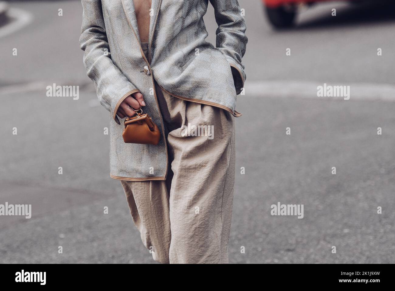 Milan, Italy - February, 24: Street style, woman wearing silver blazer jacket, beige large pants, a brown shiny leather micro First handbag from Fendi Stock Photo