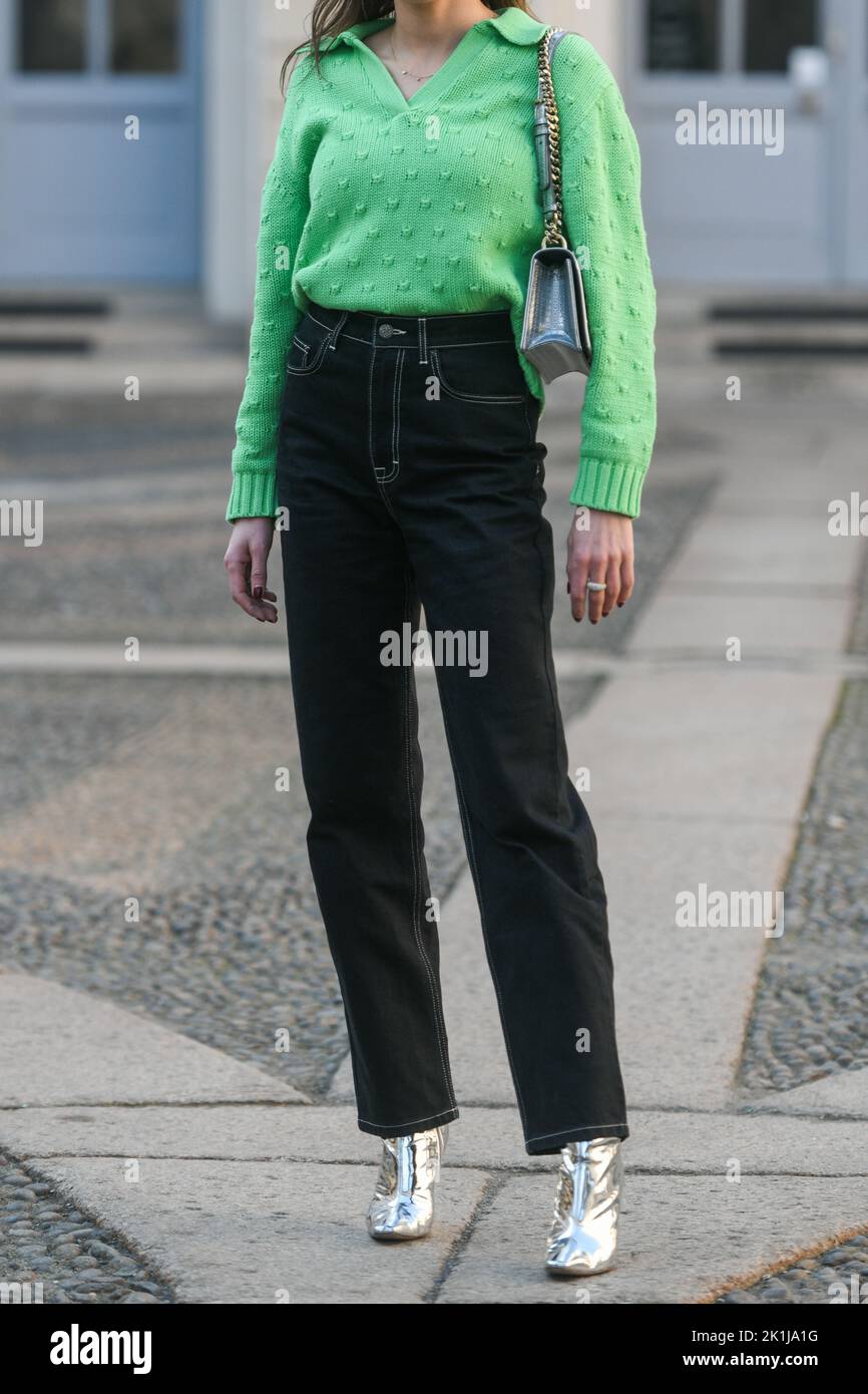 Milan, Italy - February, 25: Street style, woman wearing green V-neck polo pullover, a silver shoulder bag from Dior, high waist black denim large pan Stock Photo