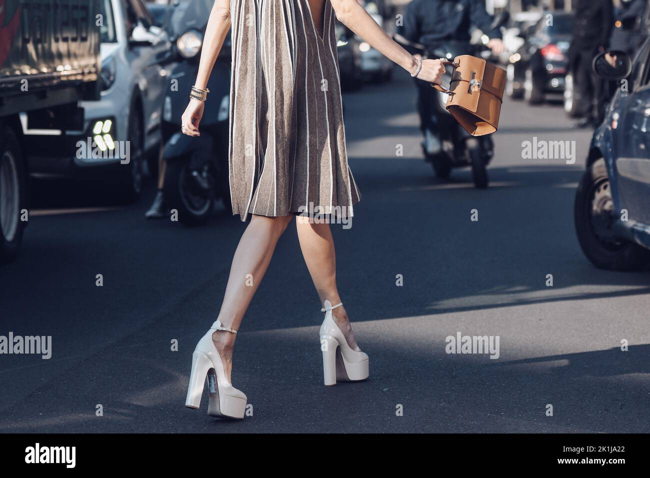 Milan, Italy - February, 25: Street style, woman wearing a beige and brown accordion halter-neck short dress, a brown shiny leather handbag, white var Stock Photo