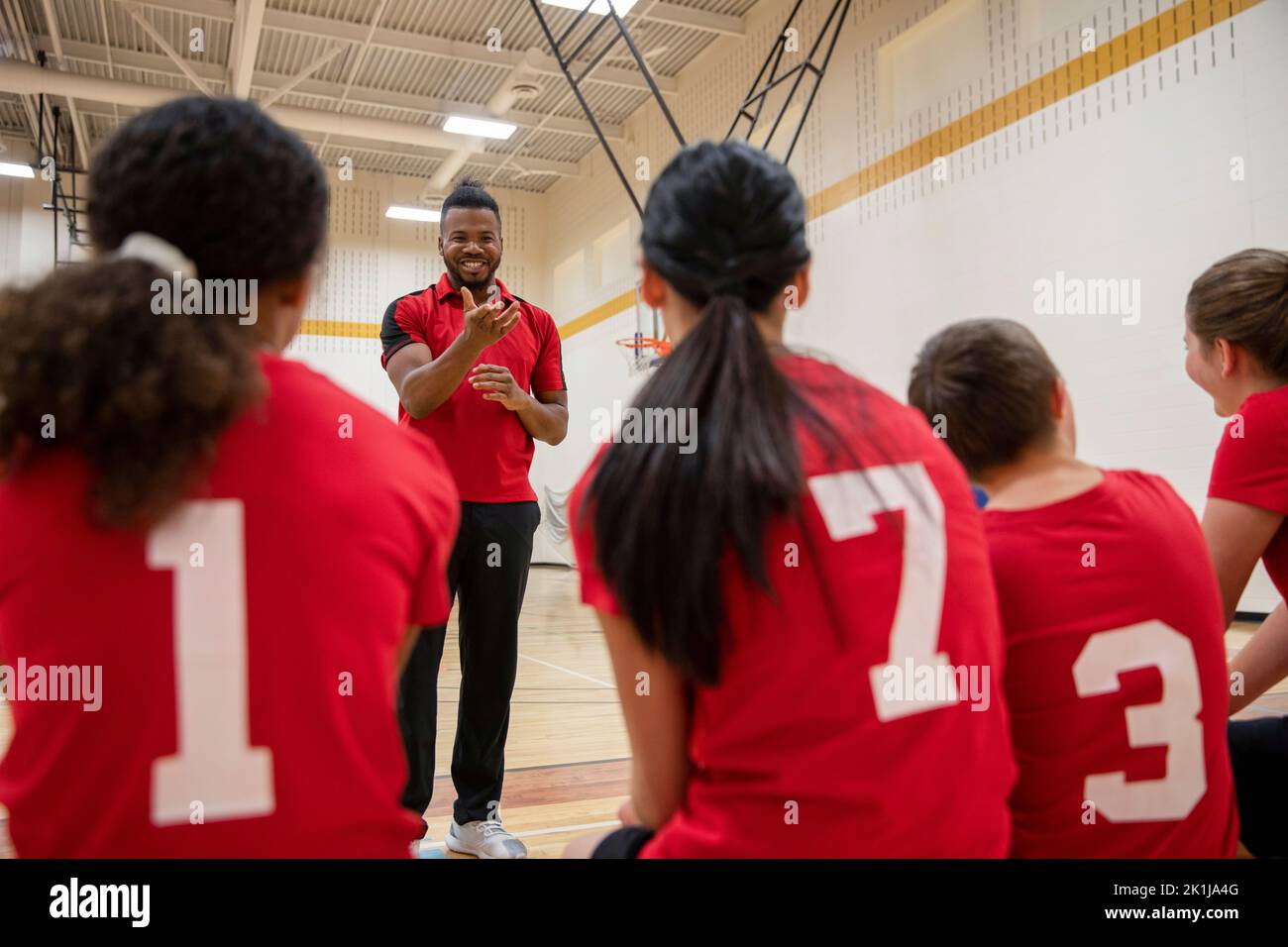 Happy male junior high basketball coach talking to students in